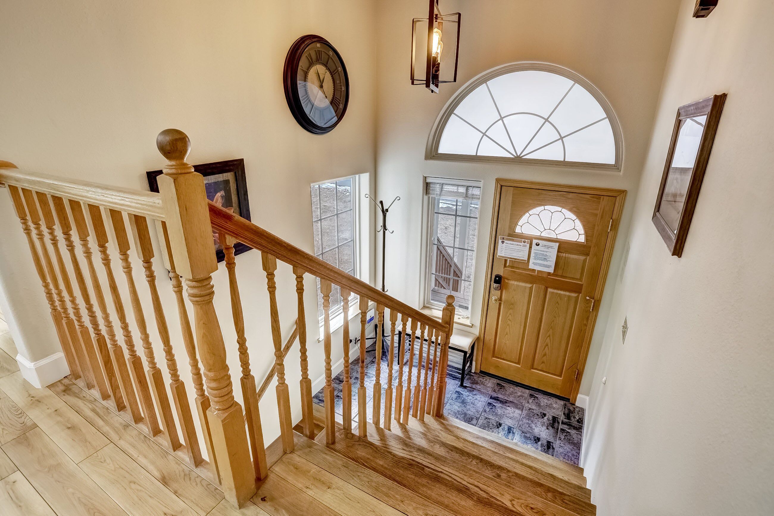 A wooden staircase with a handrail, a clock, and a door with a window above it.