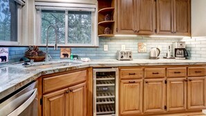 A kitchen with wooden cabinets, a built-in oven, a window with a view of trees, and a countertop with various appliances.