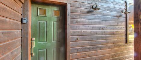 Une porte en bois avec une poignée verte et un trou de serrure, une sonnette métallique et une petite boîte aux lettres fixée au mur.