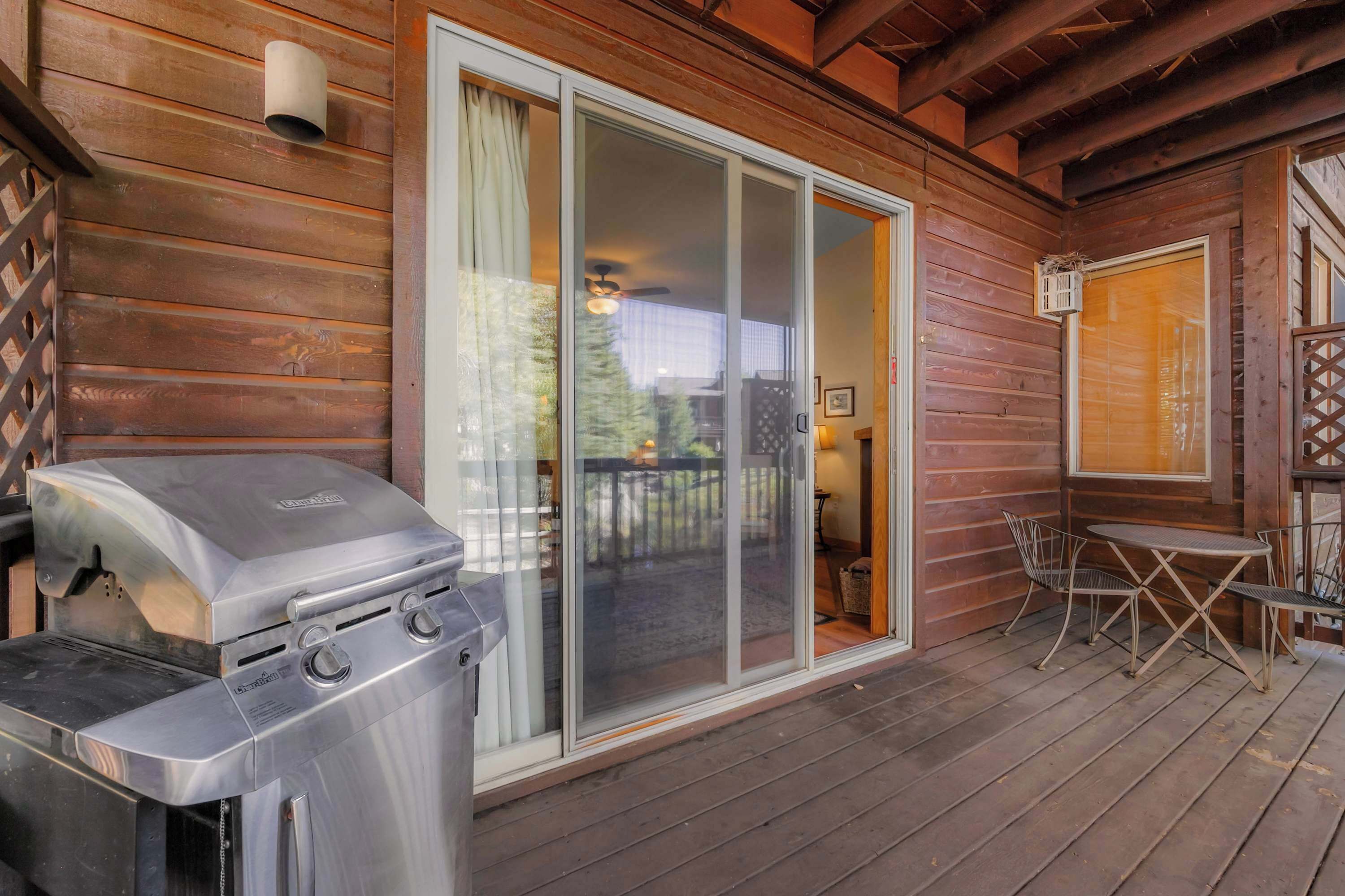 A wooden deck with a barbecue grill, sliding glass doors, and a small table with chairs.