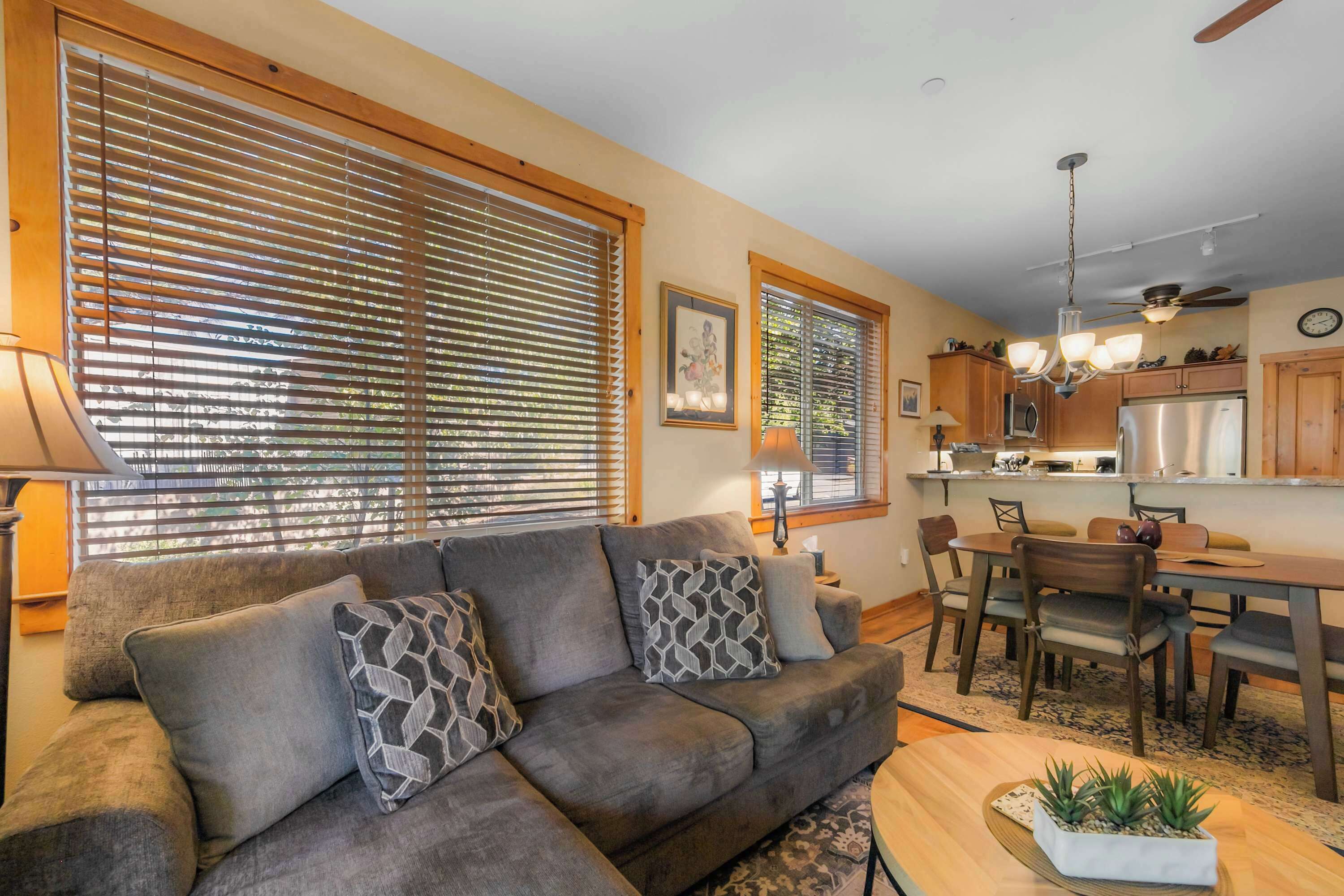 A living room with a sofa, patterned cushions, a coffee table with plants, and a dining area with chairs and a table.