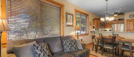 A living room with a sofa, patterned cushions, a coffee table with plants, and a dining area with chairs and a table.