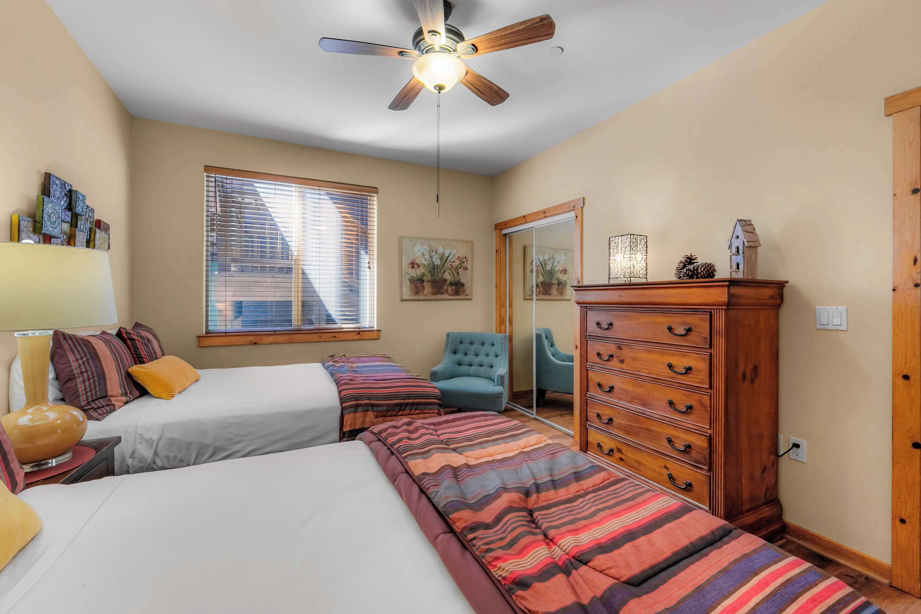 A bedroom with two beds, a ceiling fan, a dresser, a chair, and a window with blinds.