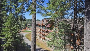 A lodge with multiple wooden balconies, a central staircase, and a view of a forested area. - A Golden Getaway Pool, Hot Tub, Tennis, & More (Truckee)