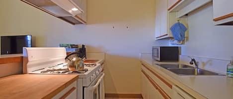 A compact kitchen with a stove, oven, microwave, and sink.