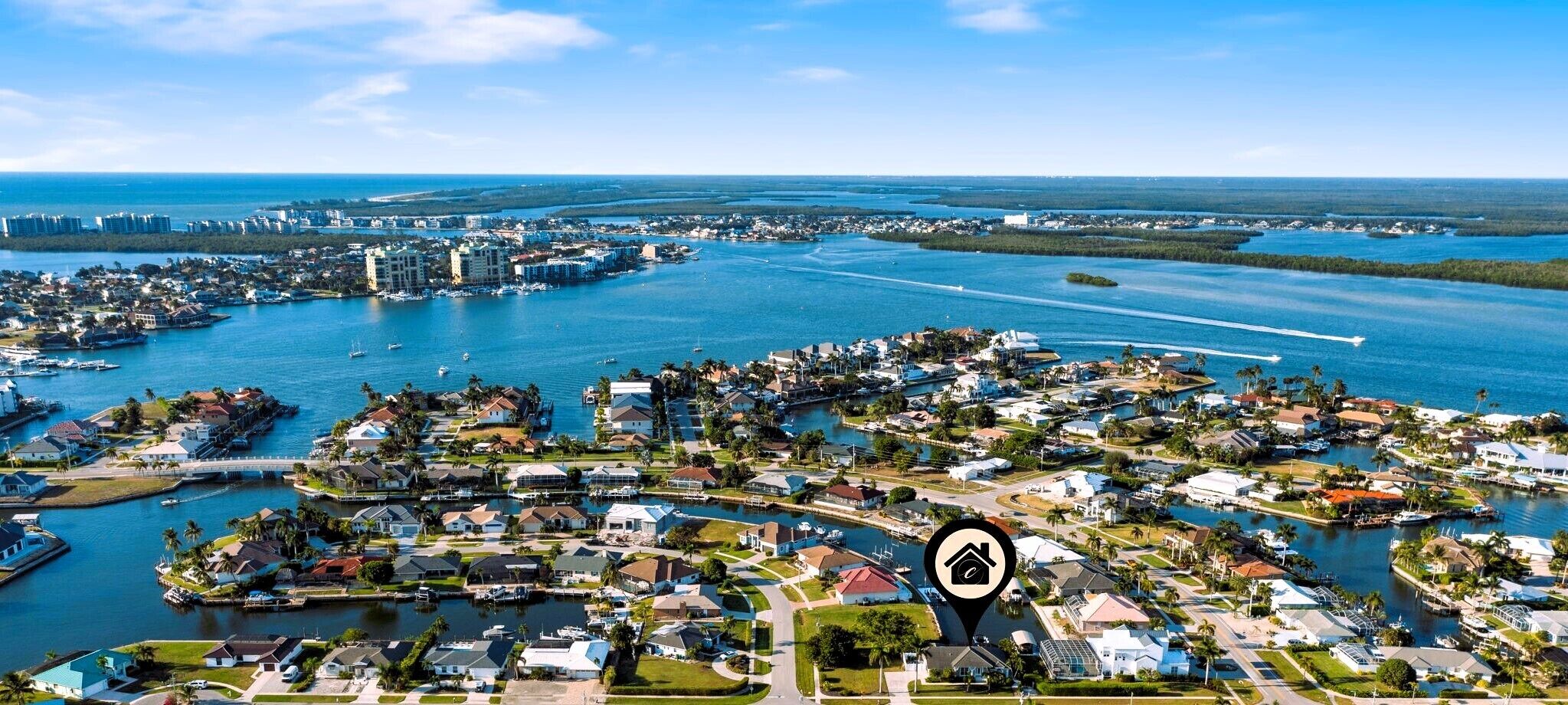 An aerial view of a coastal residential area with houses, boats, and a marina.