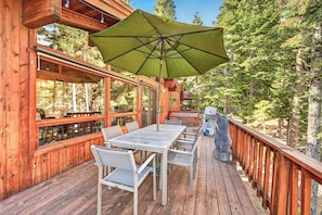 A wooden deck with a table and chairs, an umbrella, and a grill.
