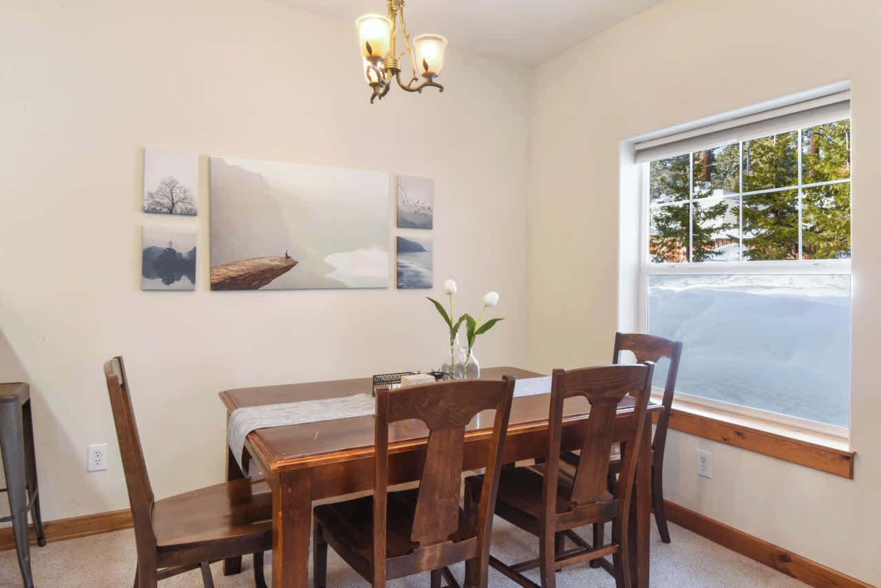 A dining area with a wooden table and chairs, a chandelier, and a window with a view of trees.