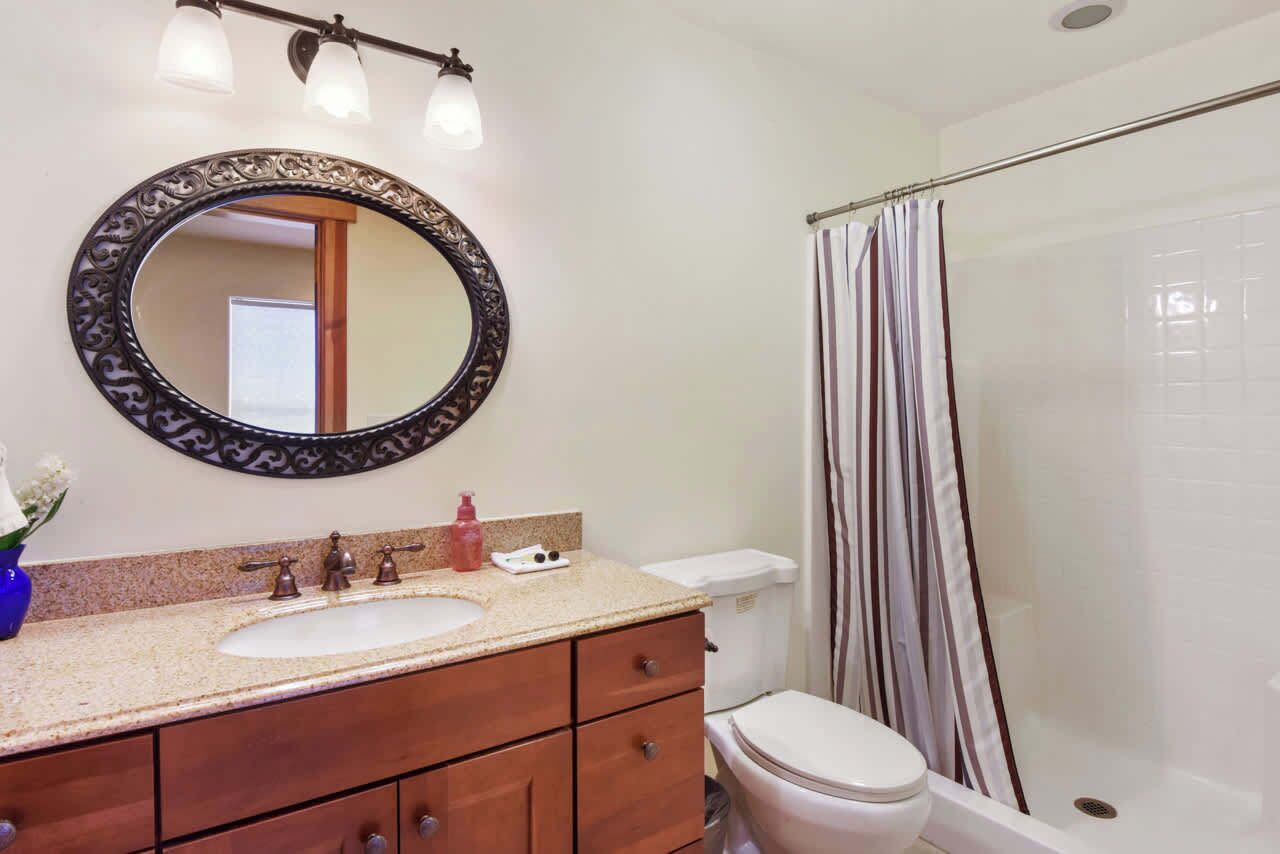 A bathroom with a round mirror, a sink, a toilet, and a shower area.