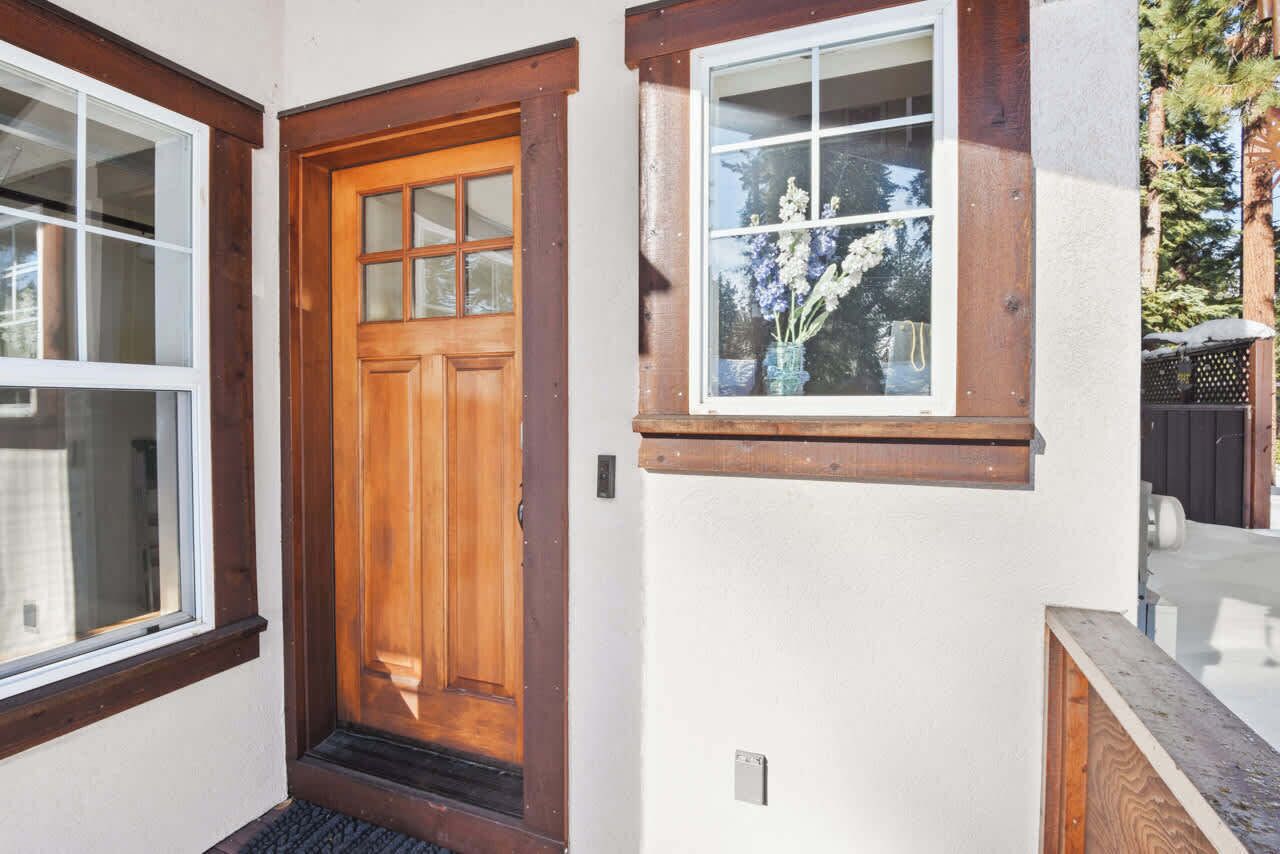 Une porte d’entrée en bois surmontée d’une fenêtre, une petite fenêtre décorée de fleurs et un banc en bois à l’extérieur.