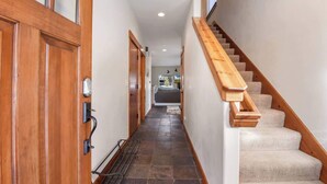 Un couloir avec une porte en bois, une poignée en métal, un sol carrelé et un escalier recouvert de moquette.