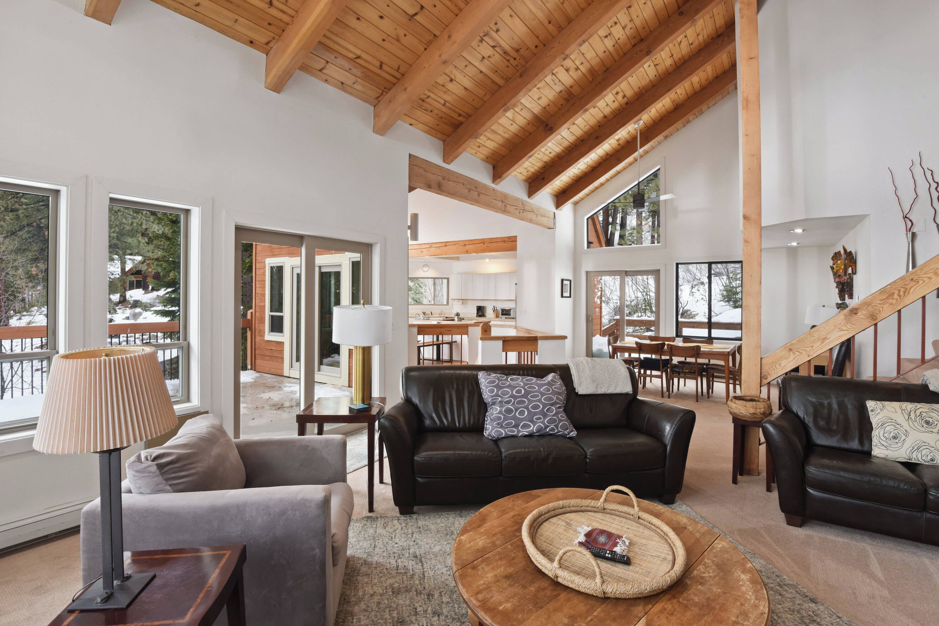 A spacious living area with a high ceiling, large windows, a fireplace, and a view of a snowy landscape.
