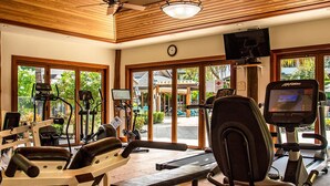 Un gimnasio con diferentes máquinas de ejercicio, amplias ventanas y un ventilador de techo.