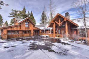 A wooden lodge with a large porch and a stone fireplace, surrounded by snow and trees. - Luxury Northstar Palace w/ Hot Tub & Games (Truckee)