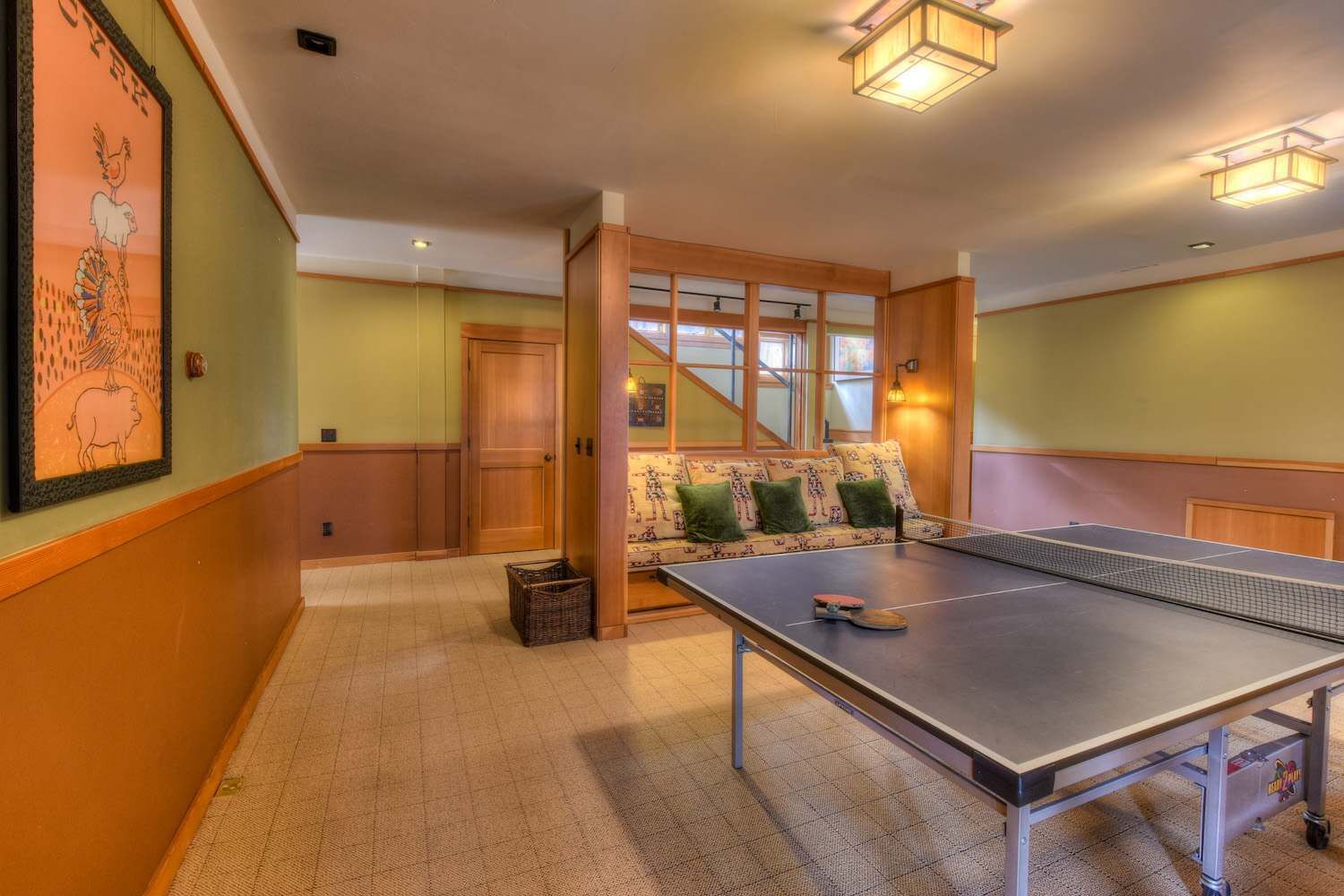 Ein Zimmer mit einem Tischtennis-Tisch, einer Couch mit gemusterten Kissen, einer Holztür und einem gerahmten Bild an der Wand.