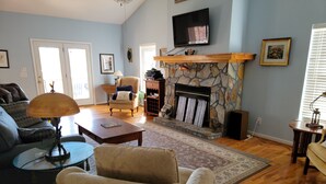 A living room with a stone fireplace, a television mounted above it, and a comfortable seating area with a sofa and armchairs. - Blues Brothers Hideaway - Lakefront - Fenced yard - Pets Welcome - Clemson 20 mi (Fair Play)
