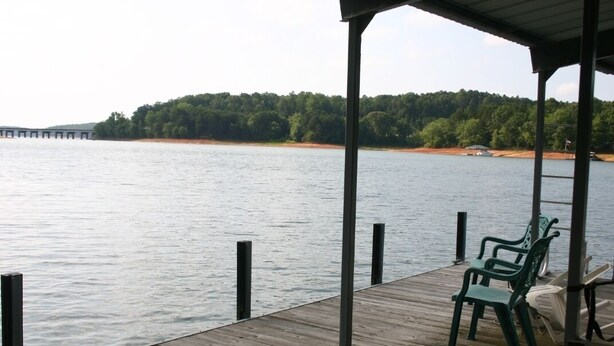 A wooden dock with chairs and a covered area overlooking a calm lake with a forested shoreline. - Blues Brothers Hideaway - Lakefront - Fenced yard - Pets Welcome - Clemson 20 mi (Fair Play)