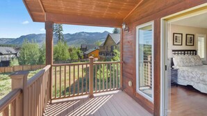 A wooden deck with a view of mountains, a bedroom with a bed and two framed pictures, and a sliding glass door. - Mule Meadows Classy, Split Level South Tahoe Home! (South Lake Tahoe)