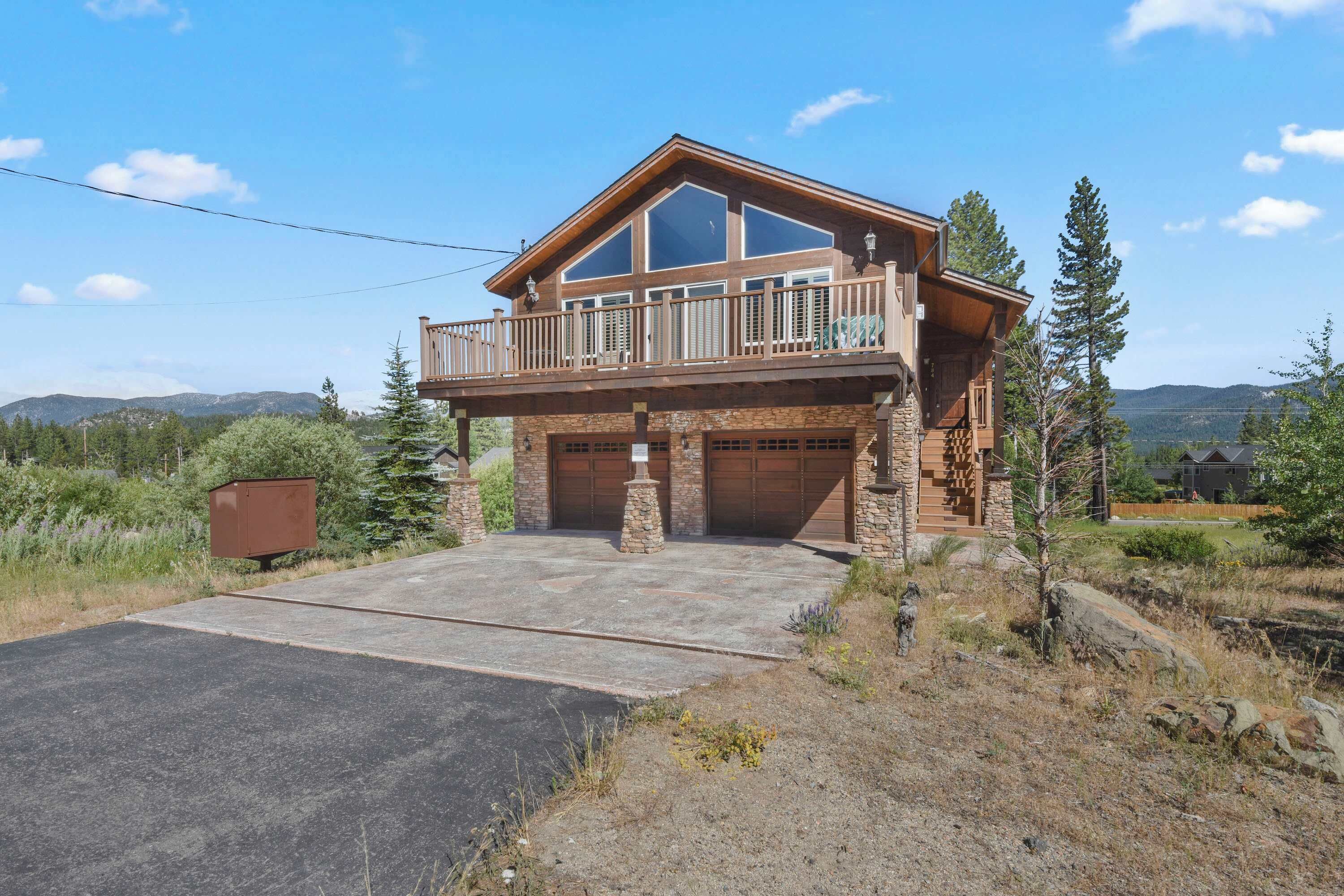 Une maison à deux étages avec un balcon, des portes de garage en pierre et une allée.