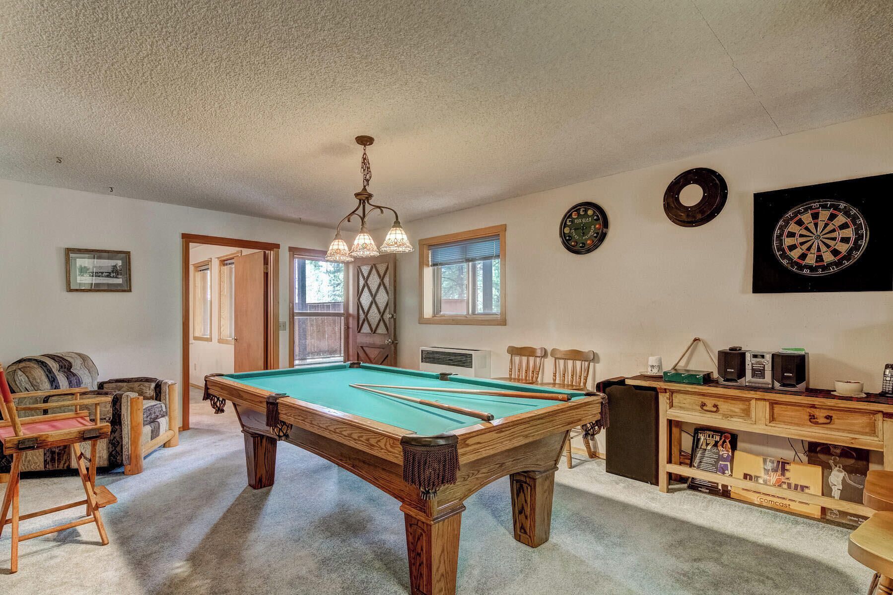 A pool table in a room with a wooden bench, a clock, and a dartboard on the wall.