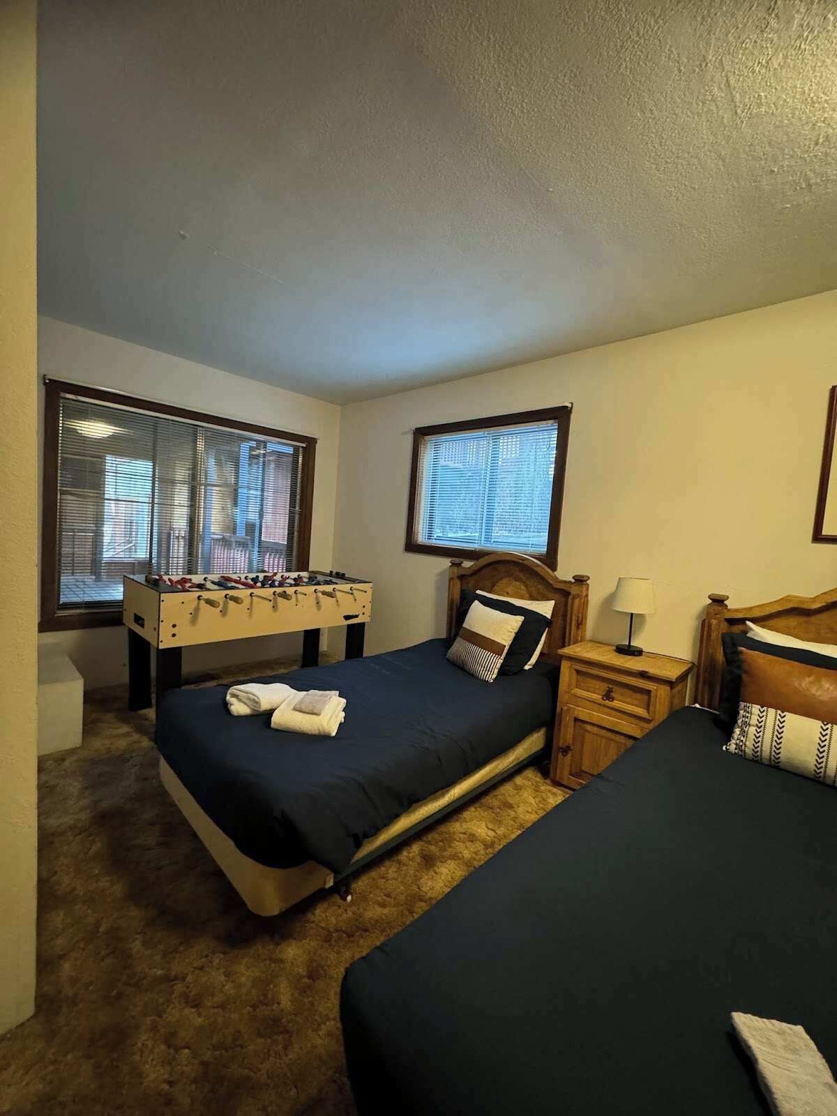 Camera d'albergo con due letti, un tavolo da calcio e due finestre.