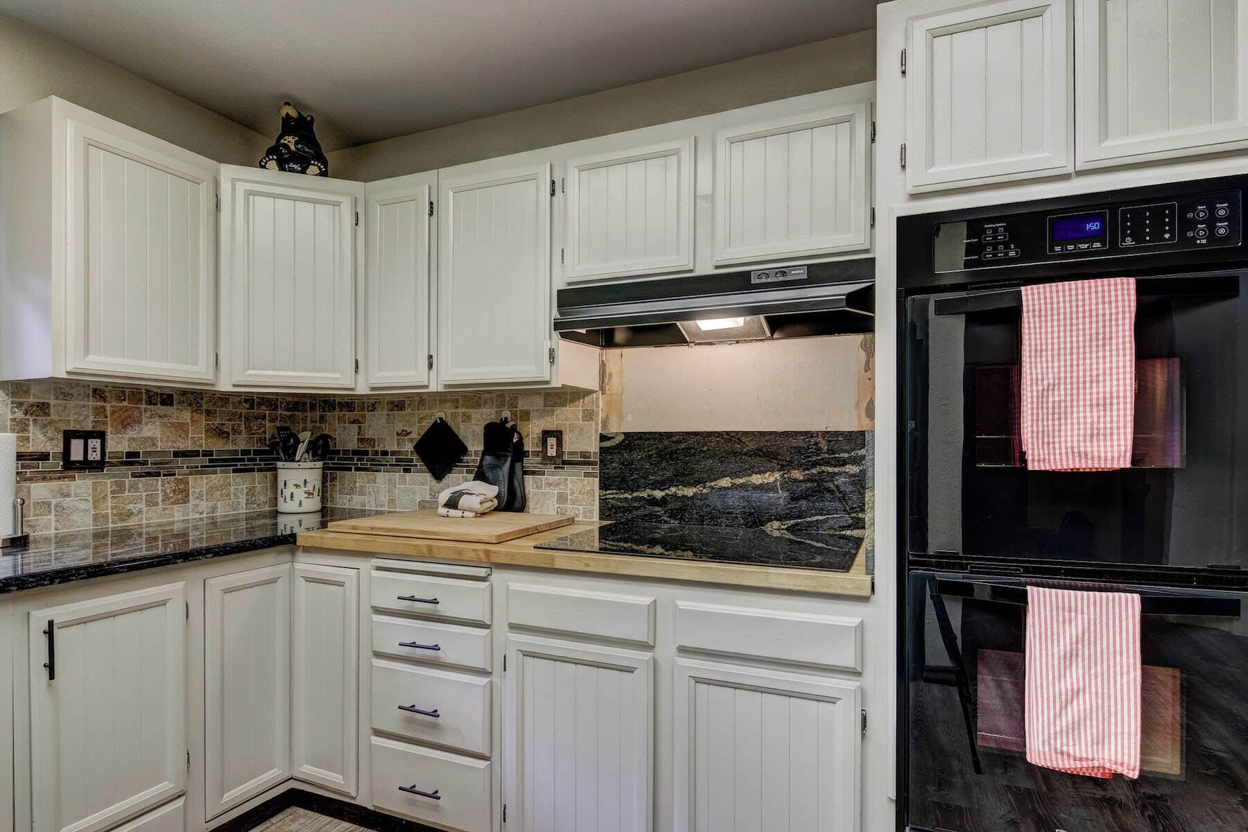 A kitchen with white cabinets, a black oven, and a tiled backsplash.