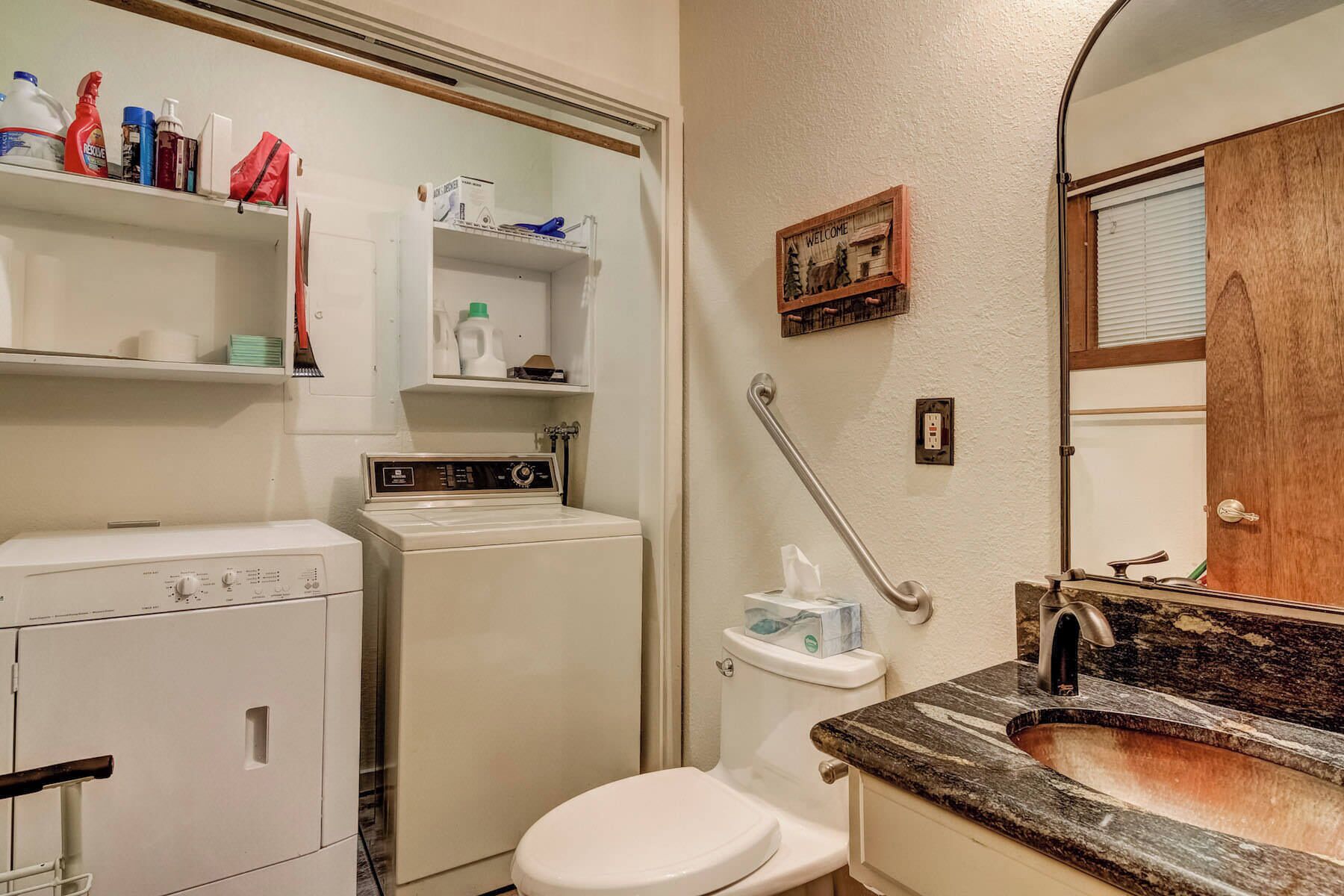 A compact bathroom with a washing machine, a toilet, and a sink with a granite countertop.