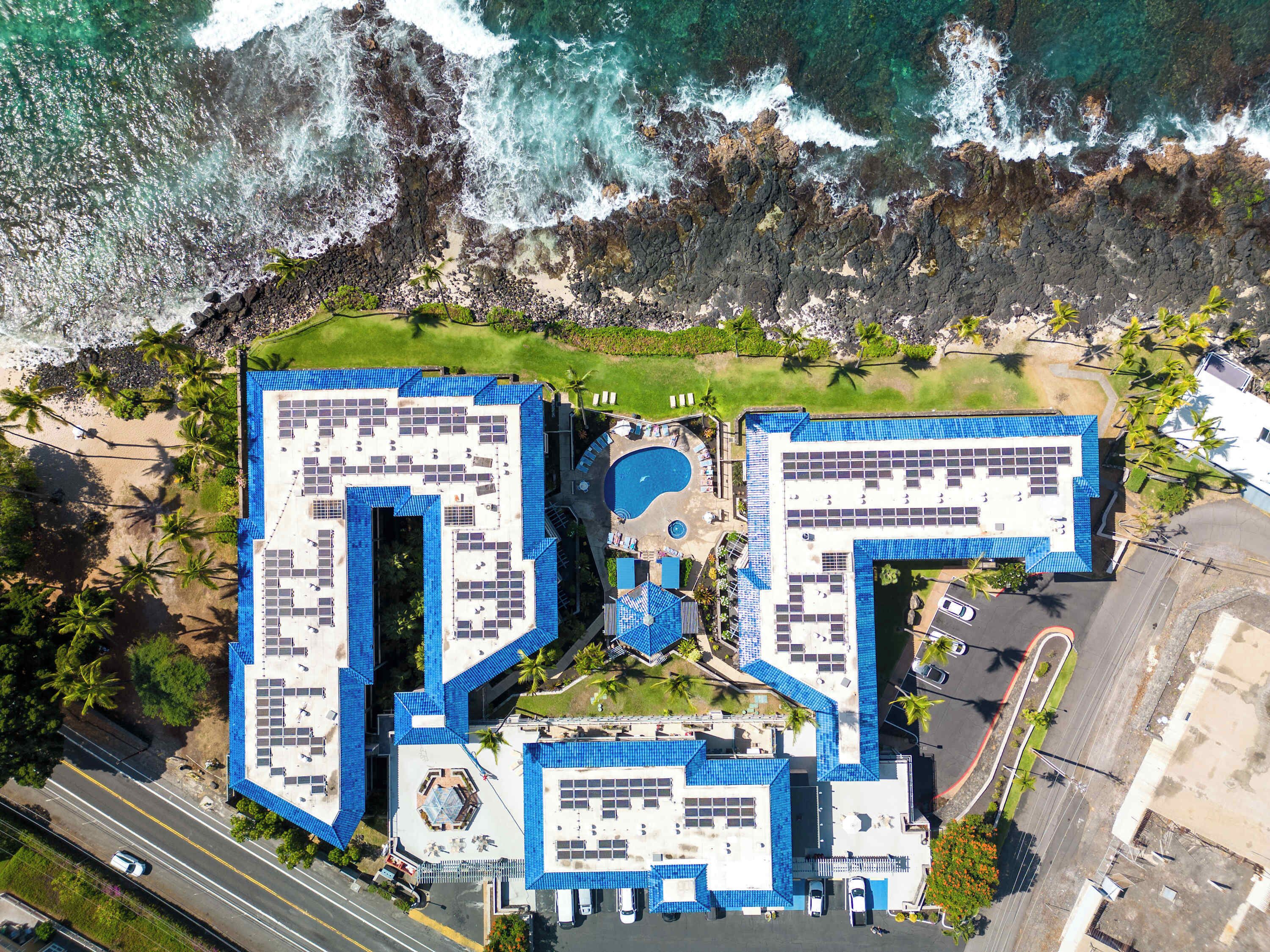 An aerial view of a resort with a pool, multiple buildings, and a beach.