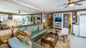 A spacious living room with a green sofa, a glass coffee table, and a ceiling fan. - Kona Reef #d31 Lanai w/ Coastal Views (Kailua-Kona)