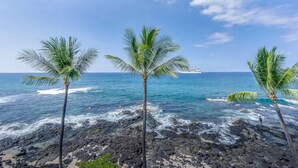 A rocky shoreline with palm trees and a cruise ship in the distance. - Kona Reef #d31 Lanai w/ Coastal Views (Kailua-Kona)