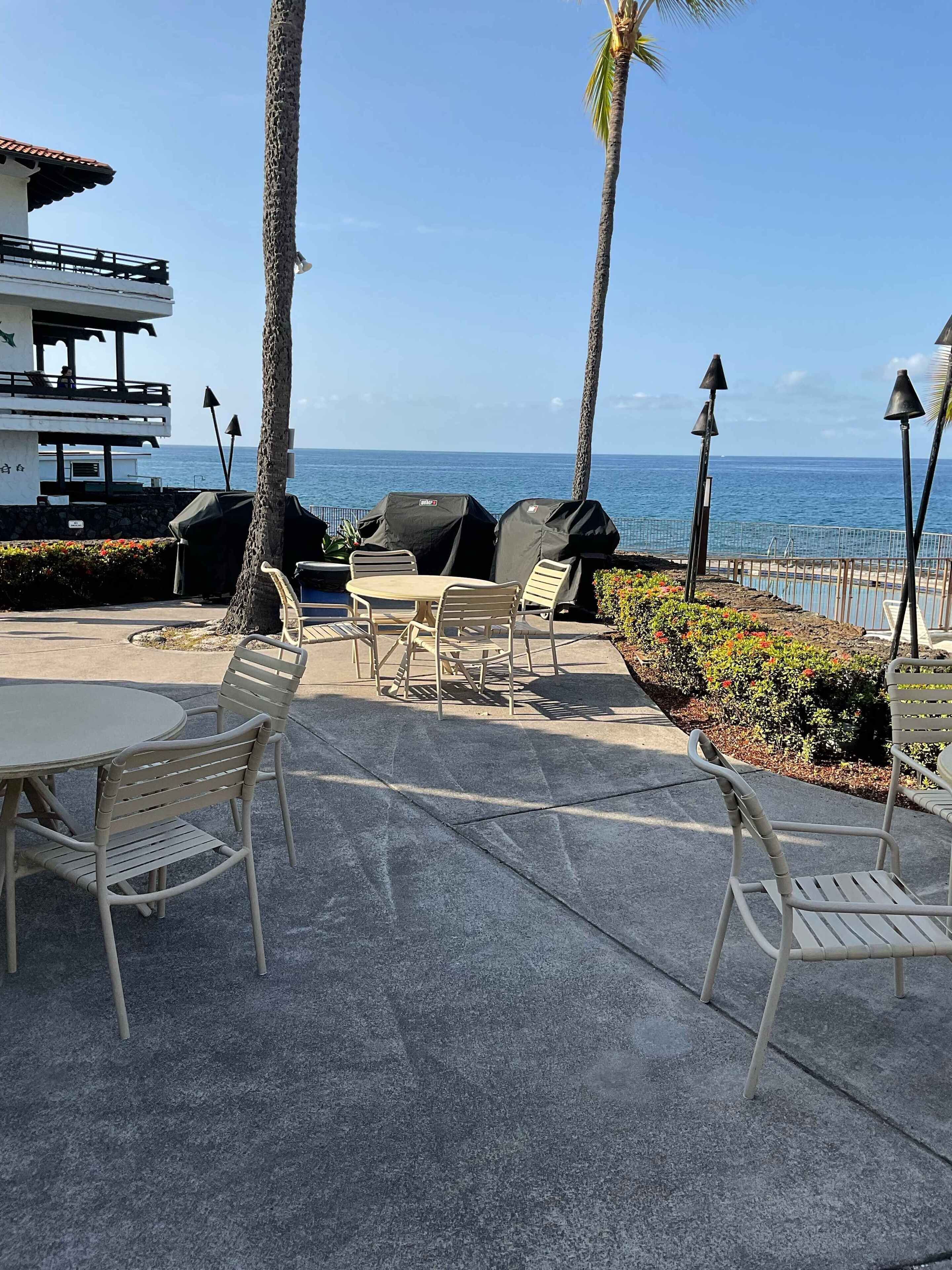 Ein Sitzbereich im Freien mit Blick auf das Meer, inklusive Tische, Stühle, Grillstationen und einem Gebäude mit Balkon.