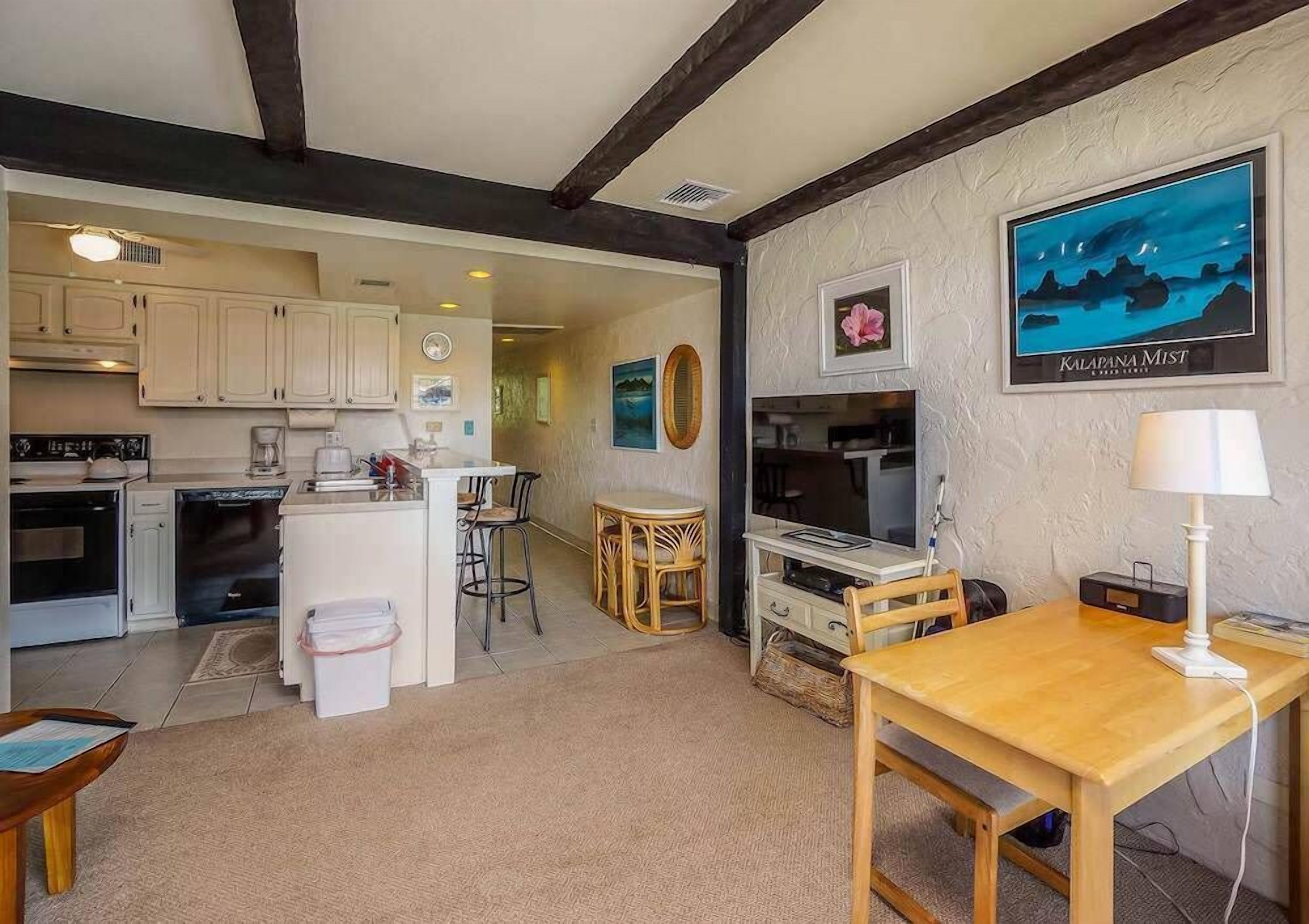 A cozy kitchen with white cabinets, a dining area with a wooden table, and a TV on the wall.