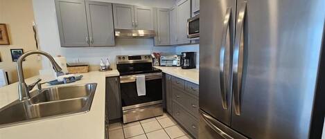 A modern kitchen with stainless steel appliances, grey cabinets, and a tiled backsplash.