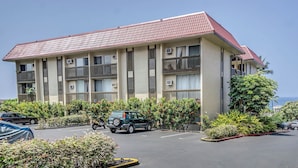 A multi-story building with a red-tiled roof, balconies, and a parking lot with several vehicles.