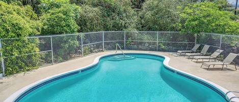 A swimming pool with a curved edge, surrounded by a metal fence, and shaded by trees.