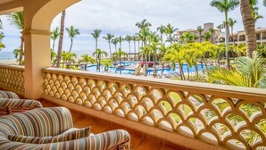Balcón de un resort con piscina, palmeras y vista al océano.