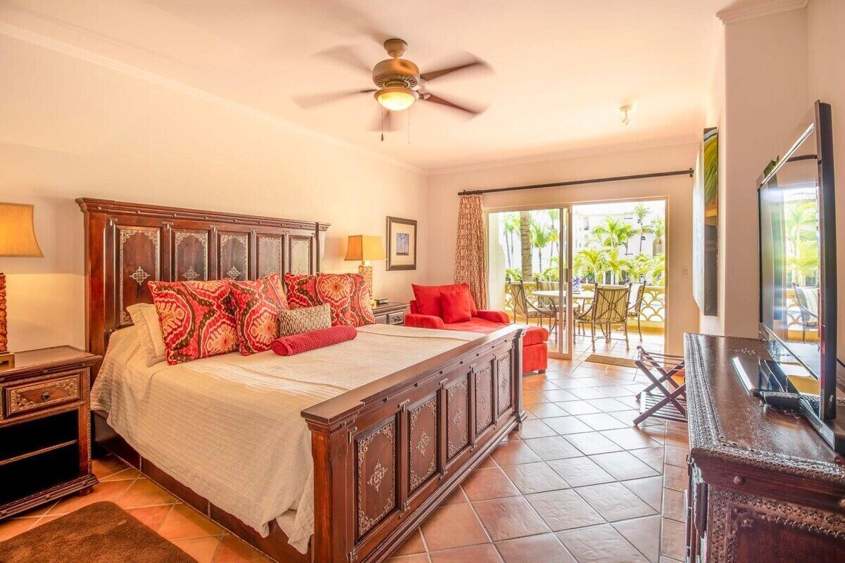 A spacious bedroom with a large bed, a ceiling fan, a balcony with outdoor furniture, and a television.