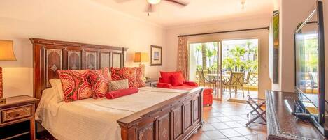 A spacious bedroom with a large bed, a ceiling fan, a balcony with outdoor furniture, and a television.