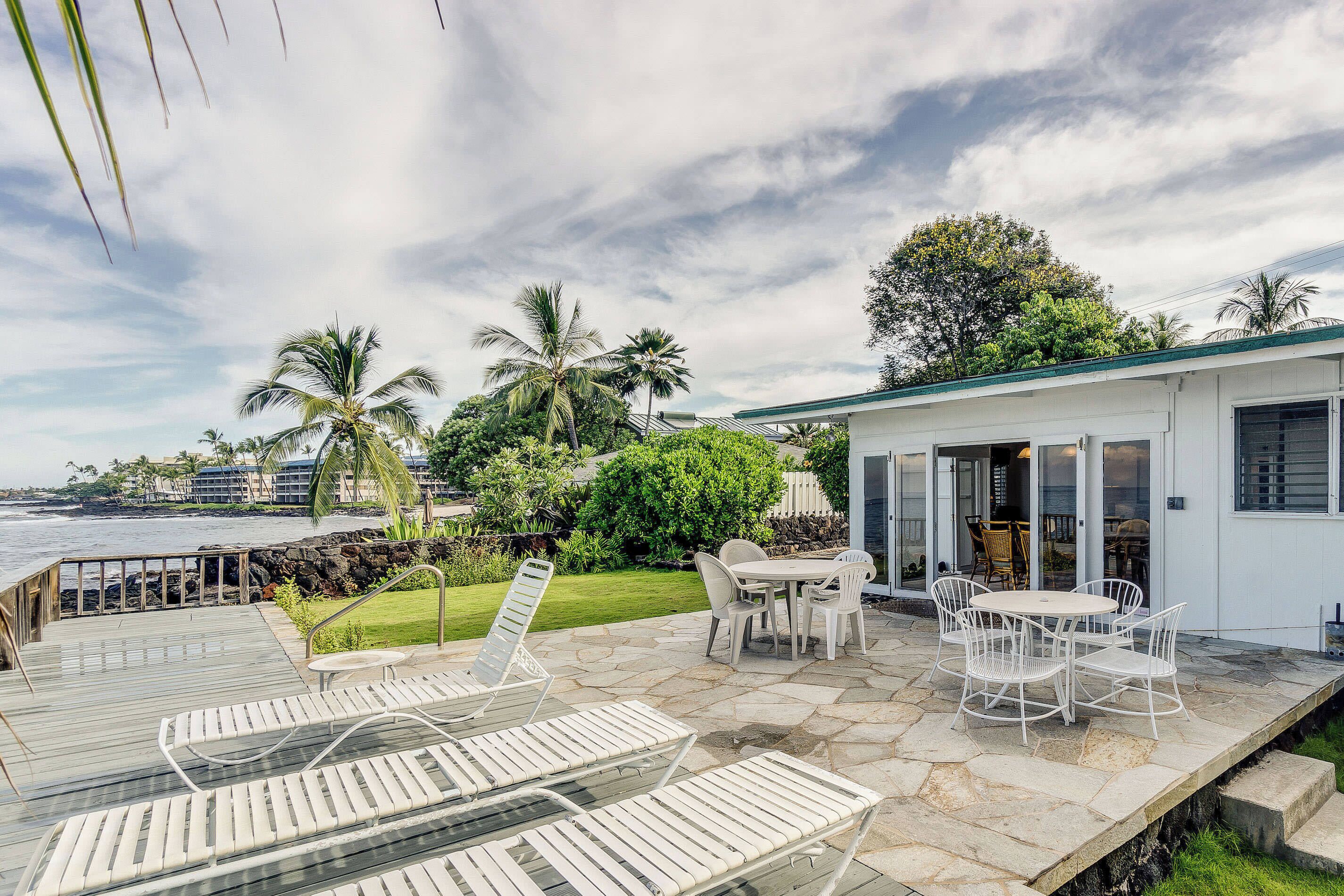 Eine Terrasse mit Liegestühlen und einem Tisch mit Blick auf Strand und Meer.