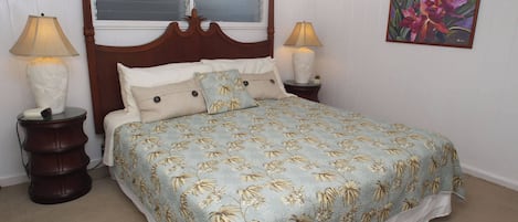 A bedroom with a four-poster bed, two bedside tables, a window with blinds, and a floral painting on the wall.