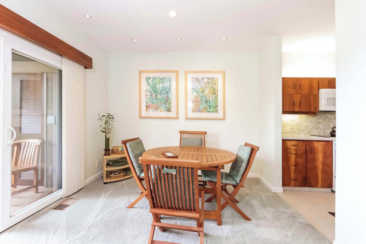 A dining area with a round wooden table and four chairs, a small side table with a vase, and two framed paintings on the wall.