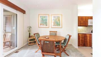 A dining area with a round wooden table and four chairs, a small side table with a vase, and two framed paintings on the wall.
