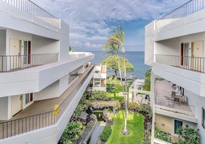 A modern hotel with multiple balconies overlooking a landscaped garden and the ocean.