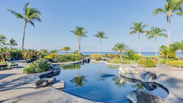 A serene pool area with palm trees and a clear view of the ocean. - Hali'i Kai 15A at the Waikoloa Beach Resort (Waikoloa)