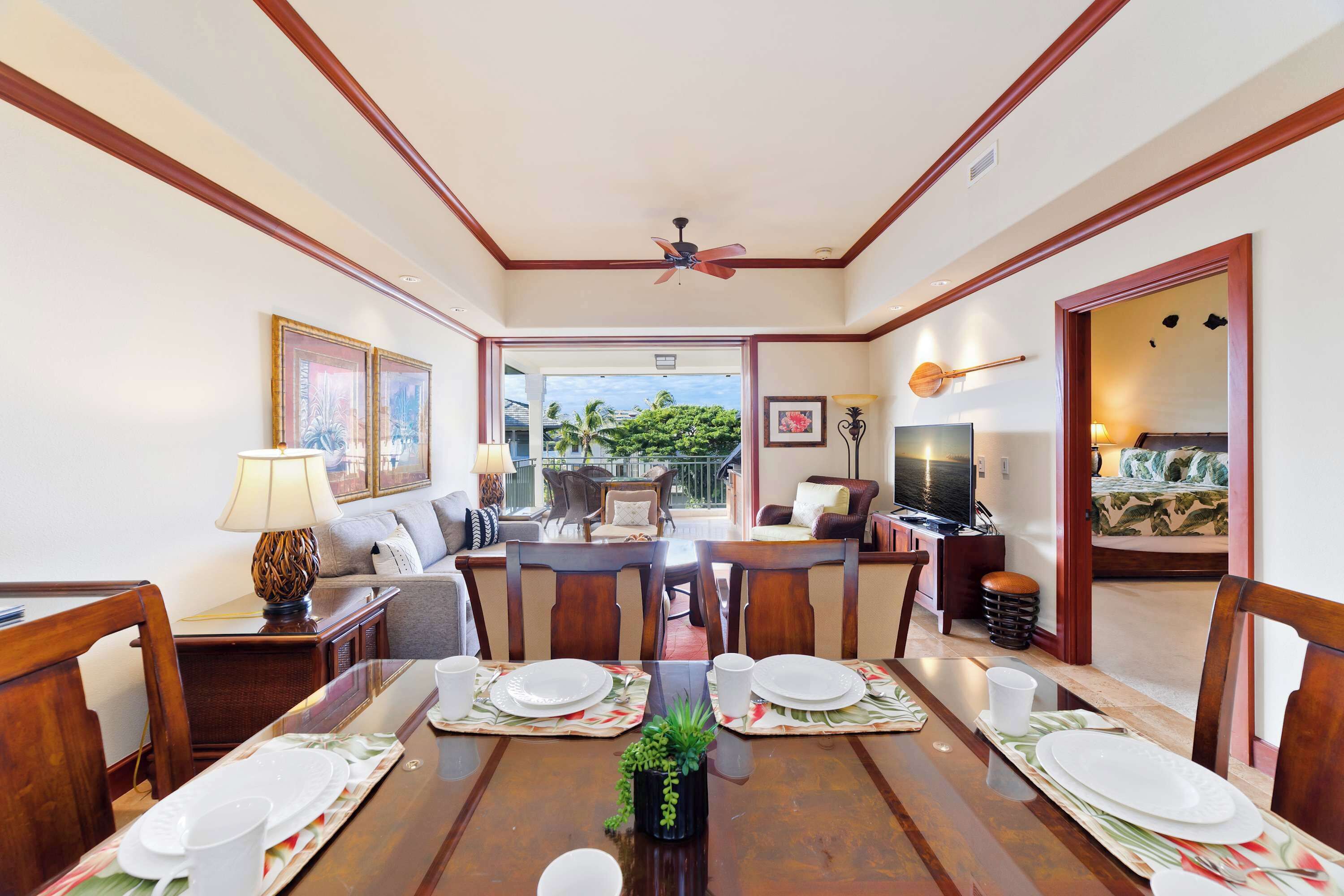 A dining area with a wooden table set for four, a ceiling fan, and a view of the outdoors.