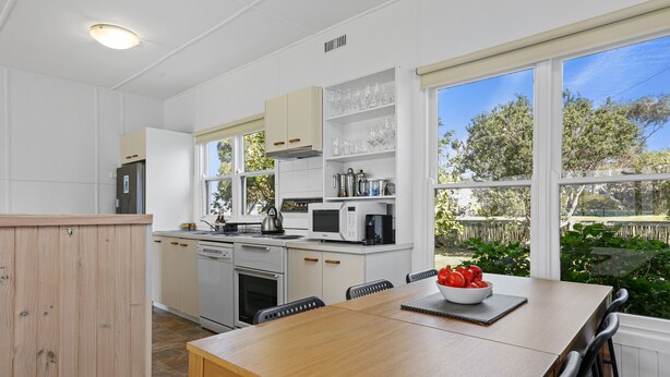A modern kitchen with white cabinets, a dining table, and a view of the outdoors. - Sea Forever (Apollo Bay)