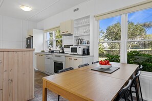 A modern kitchen with white cabinets, a dining table, and a view of the outdoors.