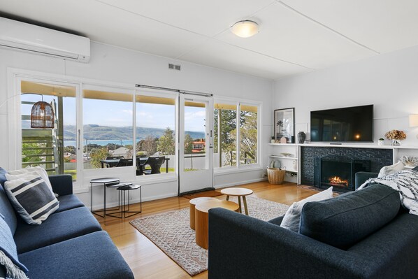 A modern living room with a fireplace, large windows, and a view of the outdoors.