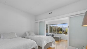A modern bedroom with two beds, a seating area, and a large window offering a view of the outdoors. - Sea Forever (Apollo Bay)