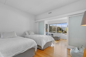 A modern bedroom with two beds, a seating area, and a large window offering a view of the outdoors. - Sea Forever (Apollo Bay)